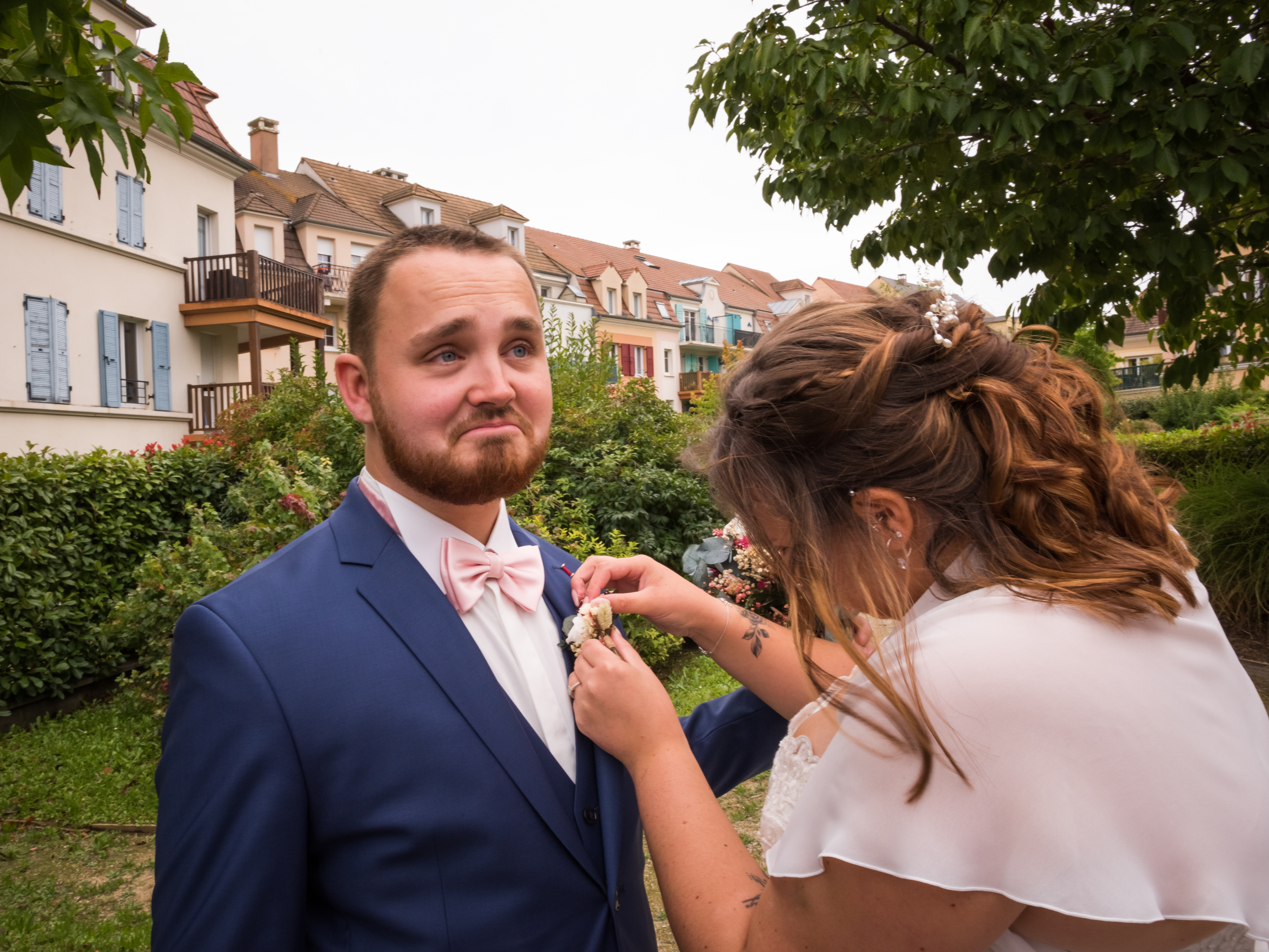 Mariage de Laurie et Valentin first look, la mariée attache une boutonnière de fleur séchées à la veste bleu du marié