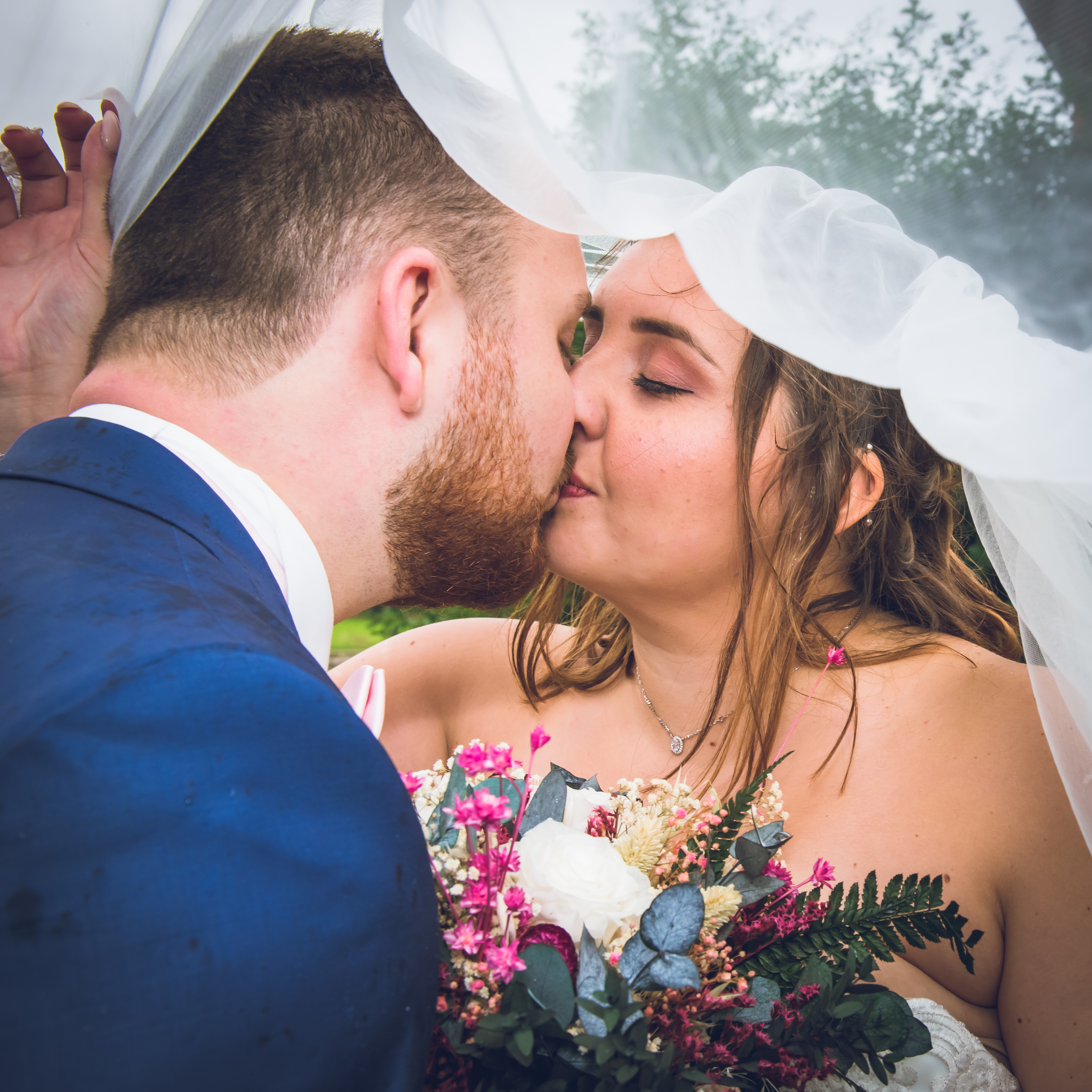 Mariage de Laurie et Valentin photo de couple sous la pluie, les mariés s'embrassent sous le voile blanc de la mariée