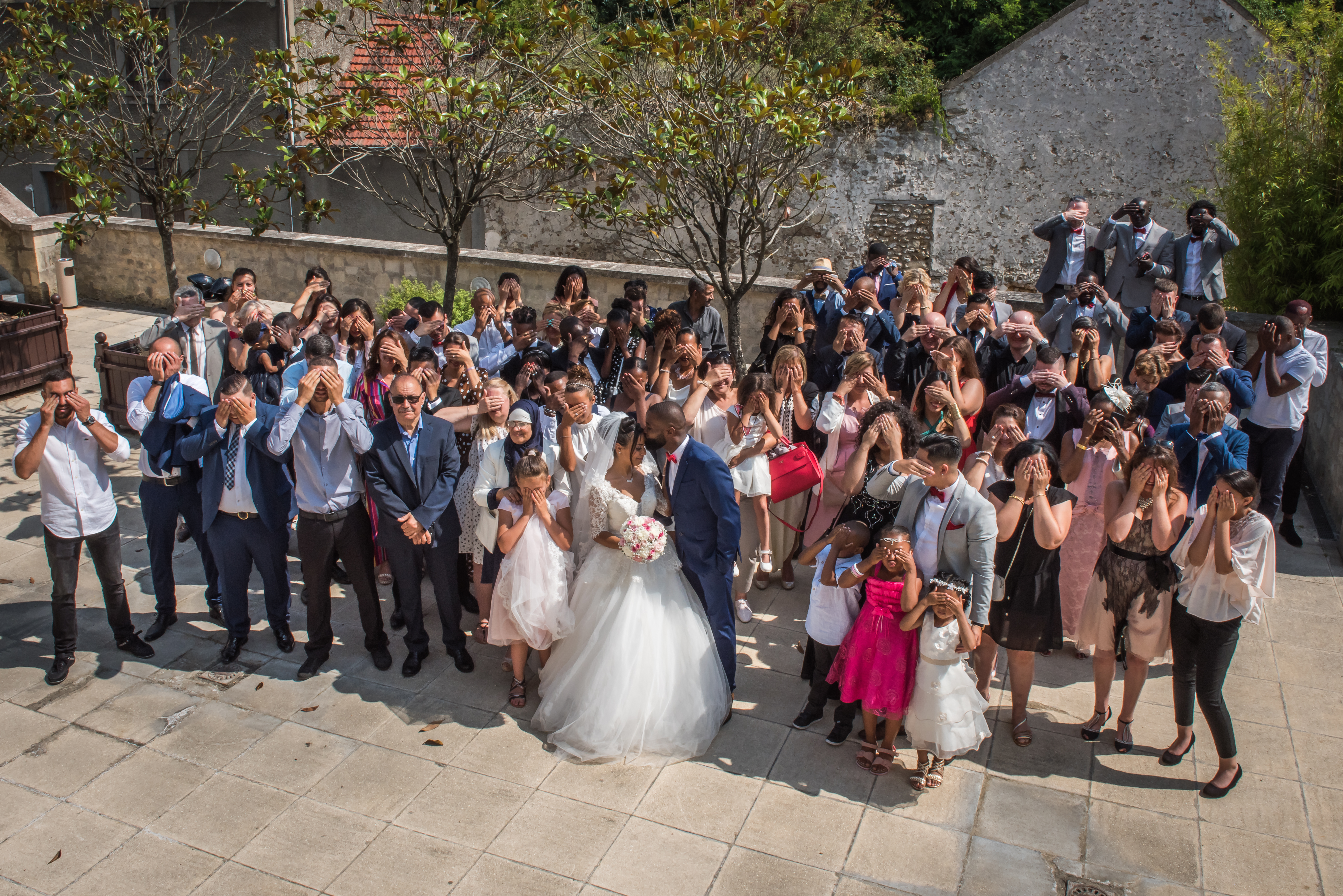 Mariage de Zara et Christy photo de groupe mairie, les mariés se font un baiser sur le front pendant que les invités se cachent les yeux