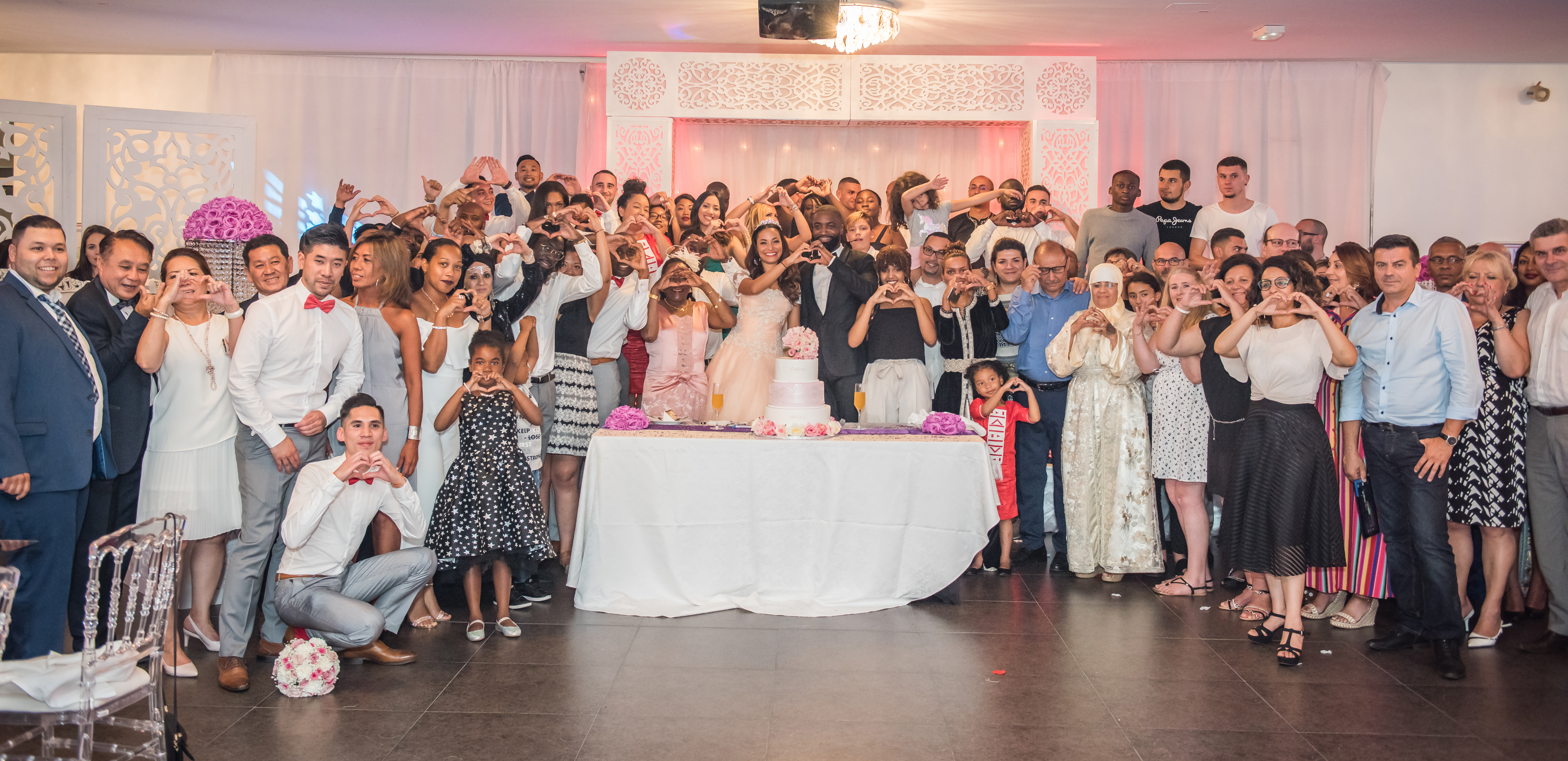 Mariage de Zara et Christy photo de groupe devant le gateau en faisant des coeurs avec les mains