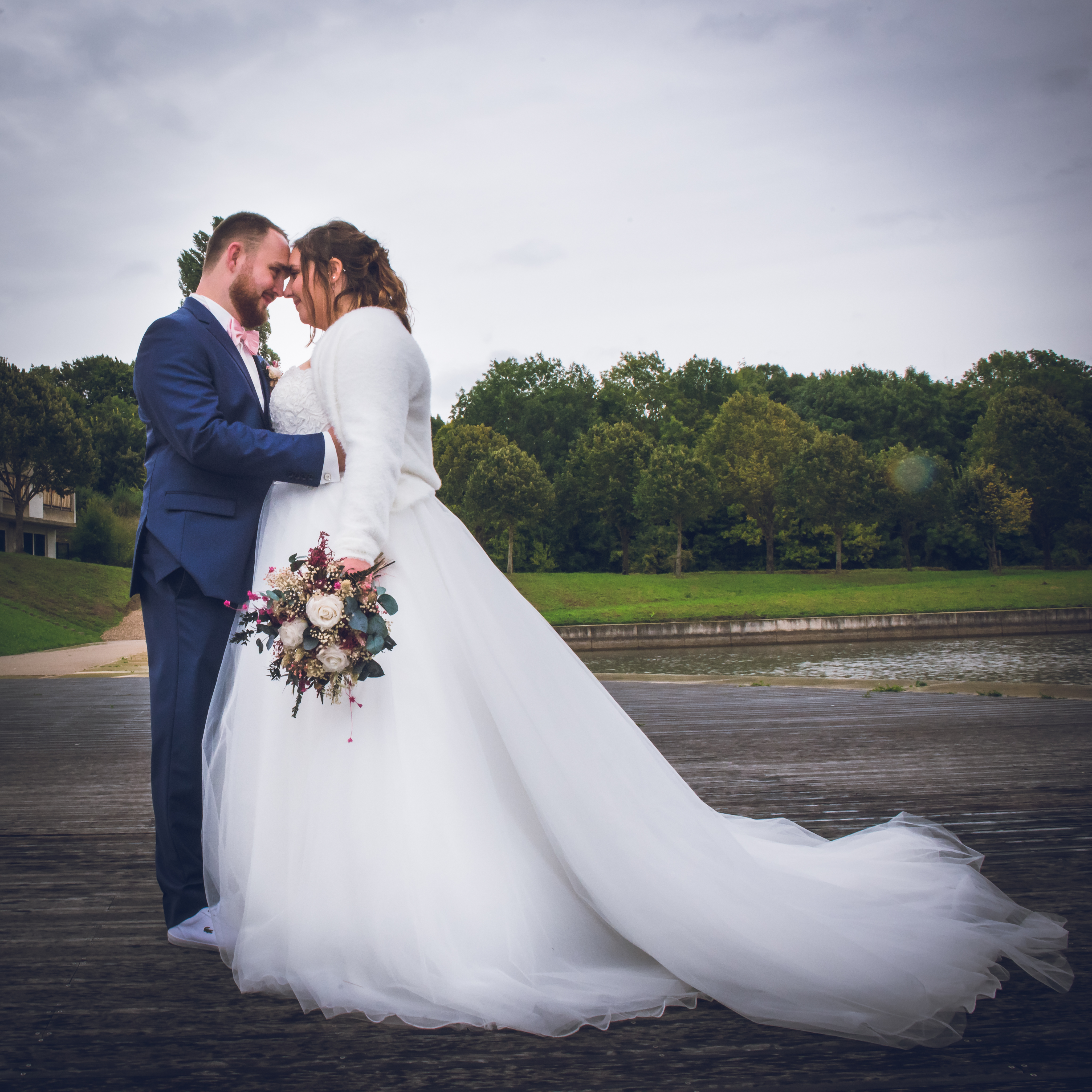 Mariage de Laurie et Valentin photo de couple, les mariés, en costume bleu et en robe blanche se tienne face à face front contre front et se regarde dans les yeux en se tenant par la taille. Le ponton est recouvert par la traine de la robe.